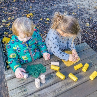 DuAS CRIANÇAS A BRINCAR COM BRINQUEDOS DE MADEIRA NUMA MESA DE MADEIRA AO AR LIVRE