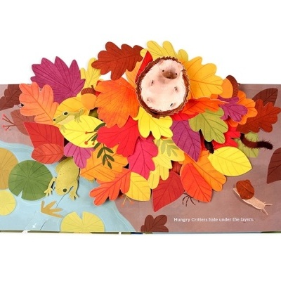 Livro infantil pop-up com folhas coloridas e criatura escondida no meio