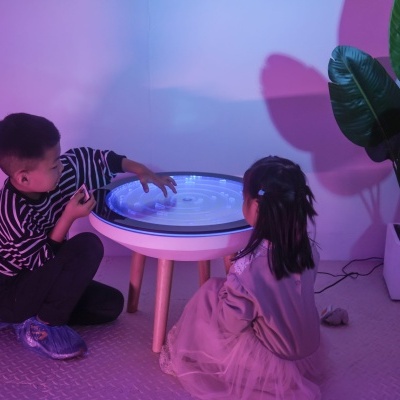 Mesa interativa branca com crianças a brincar em ambiente iluminado a roxo