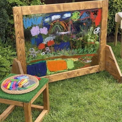 Quadro transparente com moldura de madeira pintado, cadeira de madeira com marcadores coloridos no relvado