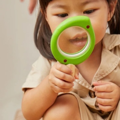 Criança segurando uma lupa verde com pontos vermelhos