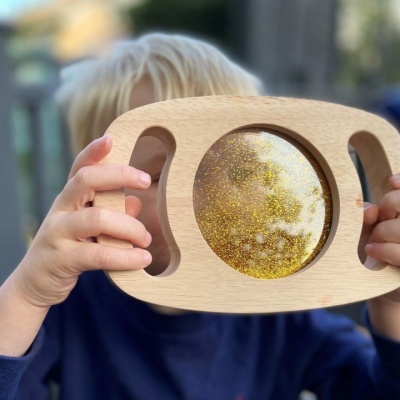 Brinquedo sensorial de madeira com glitter dourado e criança segurando