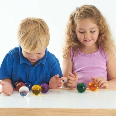 Crianças com bolinhas de vidro coloridas em cima da mesa