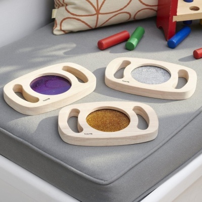 Três brinquedos de madeira com texturas coloridas sobre almofada cinza