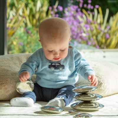 Bebé sentado com roupas azuis e meias brancas, a brincar com pedras metálicas prateadas empilhadas