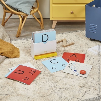 Cartões educativos com letras e lousa num tapete claro em quarto com móveis coloridos