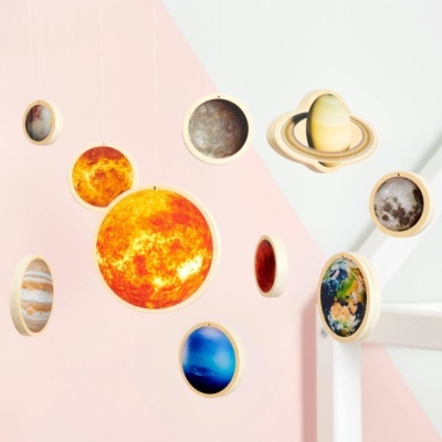 Móbile em madeira com imagens dos planetas do sistema solar suspenso numa parede rosa e branca