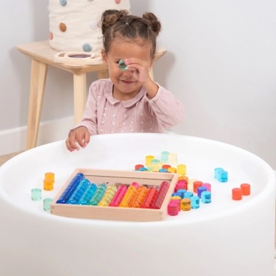 Criança a brincar com brinquedo educativo colorido numa mesa branca redonda