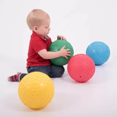 Criança brincando com bolas coloridas grandes num fundo branco