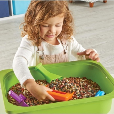 Menina a brincar com caixa verde cheia de feijões coloridos e pás de plástico