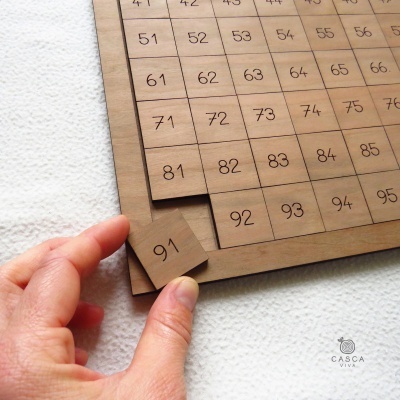 Placa de madeira com números em quadrados e uma peça amovível com o número 91