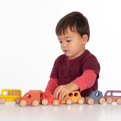 Criança a brincar com trem de brinquedo em madeira colorida.
