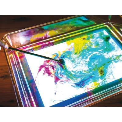 Tabuleiro transparente com líquido colorido e varinha metálica sobre madeira