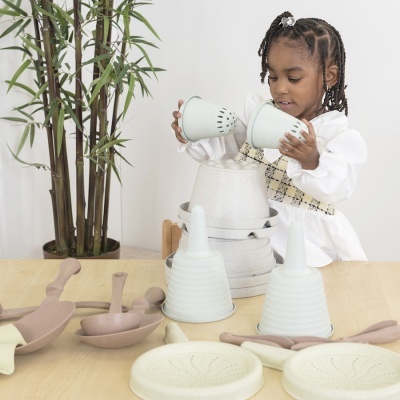 Utensílios de cozinha de brinquedo em tons pastel com criança a brincar numa mesa de madeira