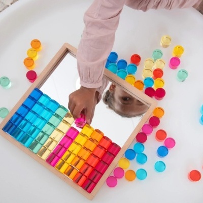 Tabuleiro com cubos coloridos e espelho e braço de criança mexendo nas peças
