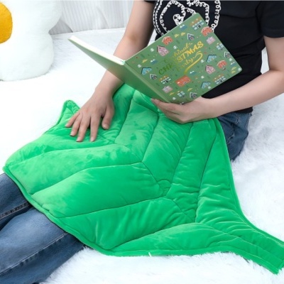 Manta verde em forma de folha com pessoa a ler livro verde de Natal