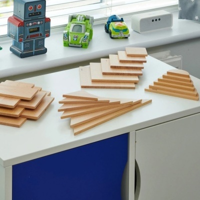 Blocos de madeira triangulares empilhados sobre mesa branca com brinquedos na janela