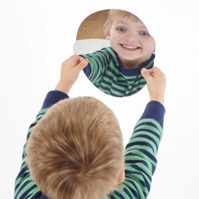 Criança segurando espelho redondo refletindo seu rosto sorridente
