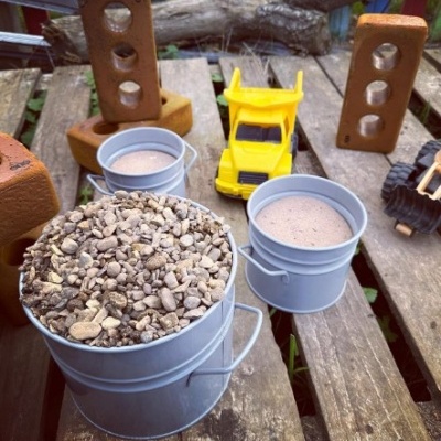 Baldes metálicos com areia e pedras pequenas em superfície de madeira, blocos de construção castanhos e brinquedos
