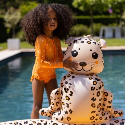 Criança com fato de banho laranja junto a piscina com brinquedo insuflável de animal com padrão leopardo.