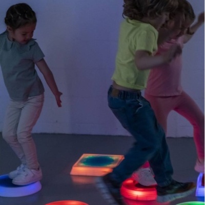 Crianças a brincar em plataformas de luz LED colorida num espaço interior.