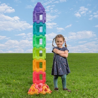 Criança ao lado de torre colorida de blocos de construção plásticos em campo de relva
