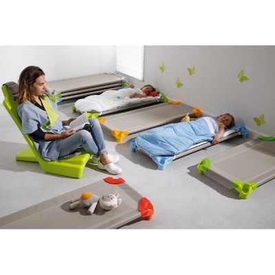 Camas infantis com crianças deitadas e adulta lendo sentada em cadeira verde