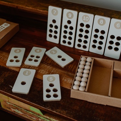 Peças de dominó brancas com furos pretos e números, caixa de papelão com bolas brancas sobre mesa de madeira