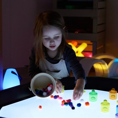 Criança com pompons coloridos numa mesa luminosa e peças de plástico