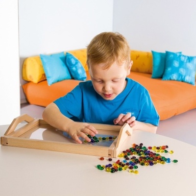 Criança a jogar com jogo de tabuleiro de madeira numa mesa branca, sofá laranja com almofadas coloridas ao fundo