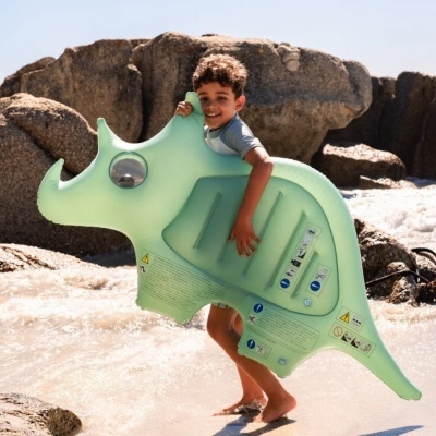 Menino na praia segurando colchão insuflável verde em forma de rinoceronte