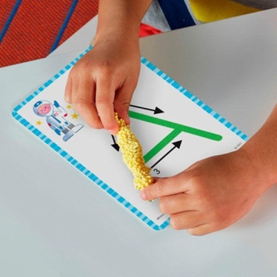 Mãos infantis segurando textura amarela sobre papel com letra A e astronauta