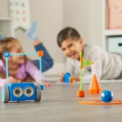 Carro robô azul com rodas e olhos grandes junto a cones laranja e crianças a brincar