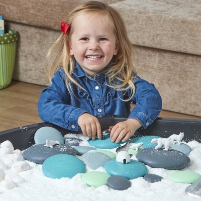 Bandeja sensorial com pedras de espuma e figuras de animais polares com criança a brincar