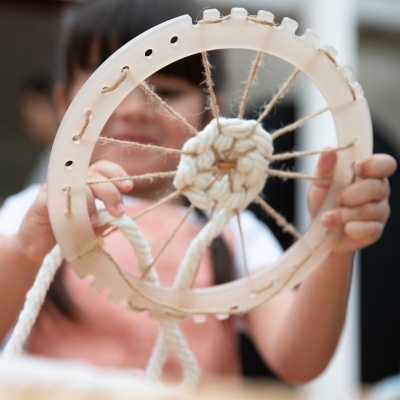 Dispositivo circular de plástico bege com corda trançada passada nos furos.