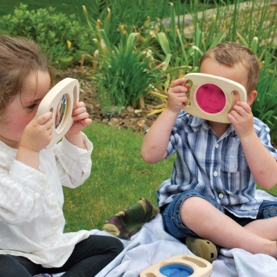 Crianças a usar brinquedos de madeira com lentes coloridas no jardim