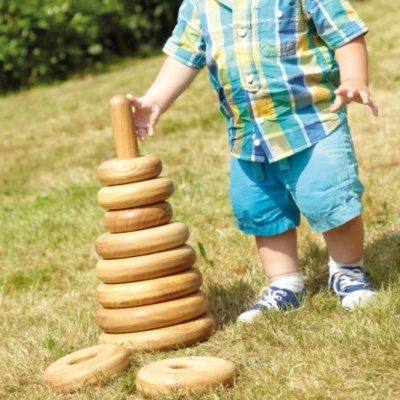 Brinquedo de madeira com argolas empilháveis e bebé a brincar na relva