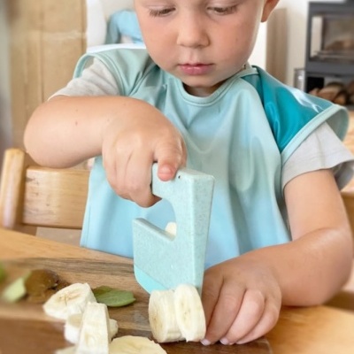 Criança a cortar banana com faca de plástico azul claro e babete azul e branco