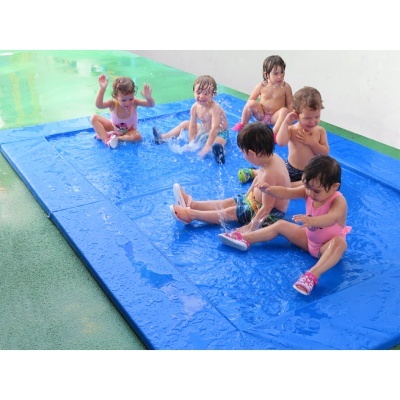 Crianças a brincar num tapete azul de água sobre relva artificial