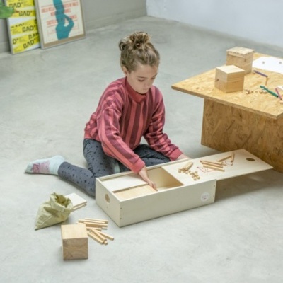 Criança a brincar com brinquedo de madeira retangular no chão ao lado de mesa baixa de madeira