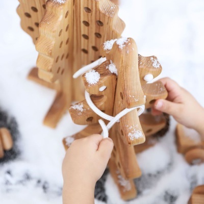 Criança amarrando cordão em pinheiro de madeira com neve artificial
