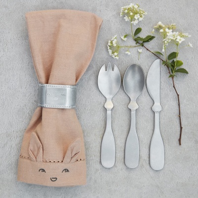 Conjunto de talheres infantis com guardanapo bege decorado e flores brancas sobre fundo cinzento