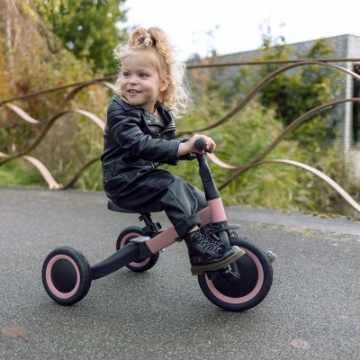 Criança num triciclo infantil preto e rosa ao ar livre