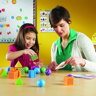Criança e mulher a brincar com blocos educativos coloridos em mesa numa sala de aula amarela