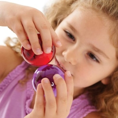 Menina de vestido roxo segurando bolas plásticas vermelha e roxa