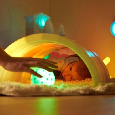 Bebé deitado num tapete sob arco iluminado atrás de uma bola luminosa