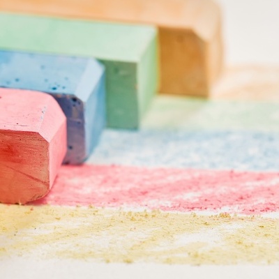 Blocos de giz coloridos alinhados sobre superfície branca com traços coloridos no chão.
