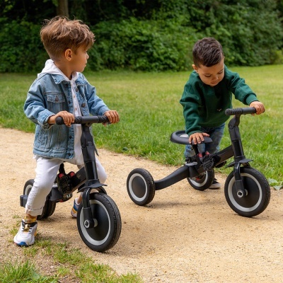 Duas crianças em triciclos pretos ao ar livre num caminho de terra