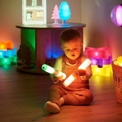 Bebé com varas luminosas coloridas sentado no chão rodeado por luzes decorativas