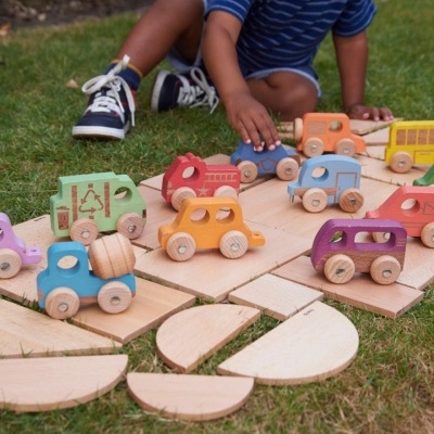 Carrinhos de madeira coloridos sobre tábuas de madeira no chão de relva com criança a brincar